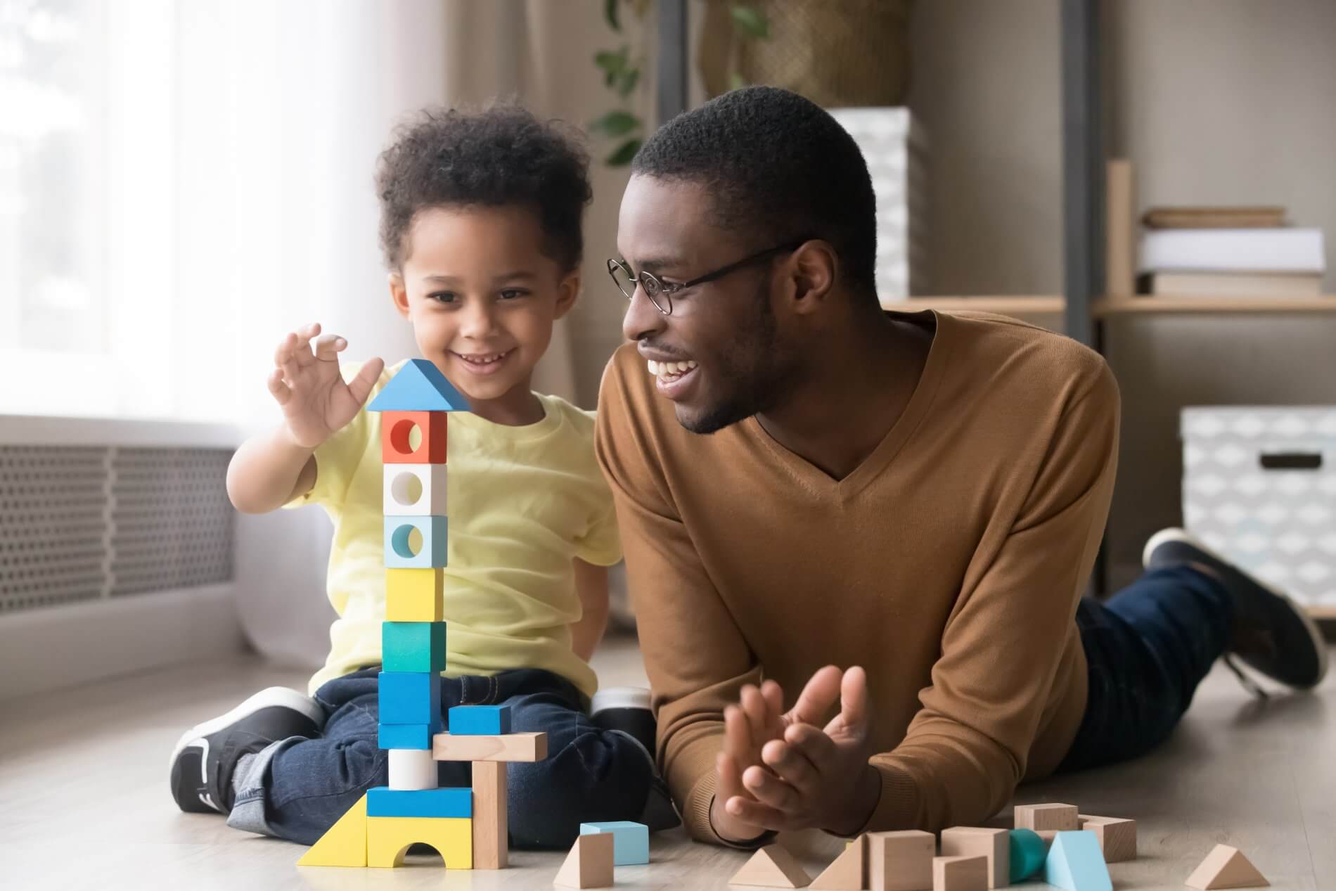 Happy little boy building wooden blocks with his father